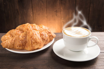 Breakfast coffee cup and croissant on wooden table