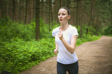 Beautiful young woman running in green park on sunny summer day