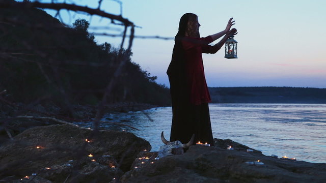 young female dressed as a witch standing on rocks near the lake
