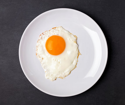 Fried egg in a white plate on the black background
