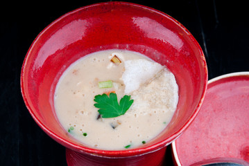 Decorated, vegetable potage served in a red cup. Vegan potage is ready for consumption, presented on a black wooden table.