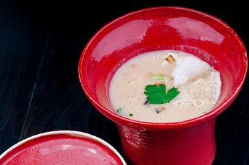 Decorated, vegetable potage served in a red cup. Vegan potage is ready for consumption, presented on a black wooden table.
