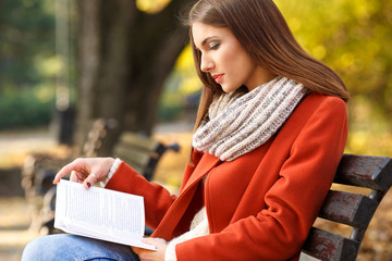 Young girl sitting on a park bench and reading a book, on a beautiful autumn day