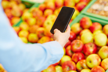 Hand hält Smartphone vor Obst im Supermarkt