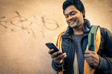 Young indian man holding mobile phone - Cheerful asian model next to old urban wall - Handsome...