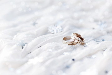 Wedding rings on white winter holiday background with sparkling silver snowflakes.