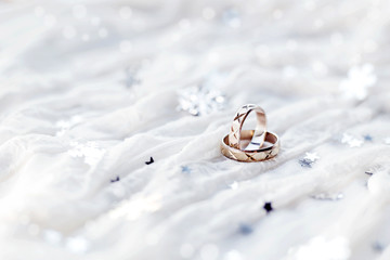Obraz na płótnie Canvas Wedding rings on white winter holiday background with sparkling silver snowflakes.