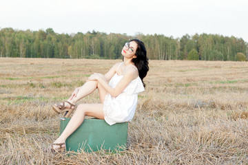 girl in a short dress sitting on an old suitcase on a background of beveled fields