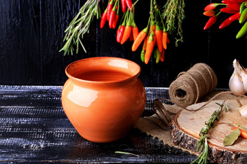 clay pot for roasting hot peppers on a dark old wooden background spices retro vintage style