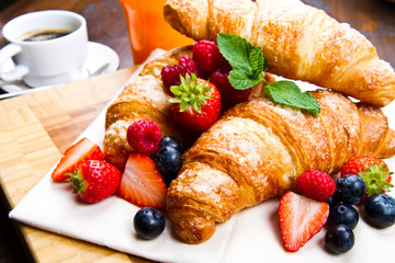 Fresh tasty croissants with berries on wooden background