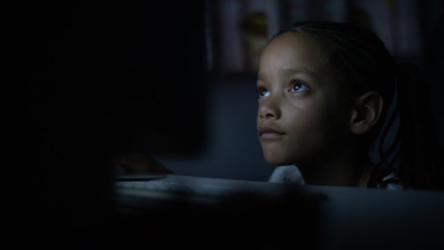 4K Young child watches a computer screen at night in the dark