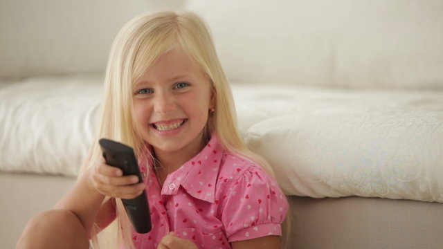 Funny little girl holding remote control smiling and showing thumb up