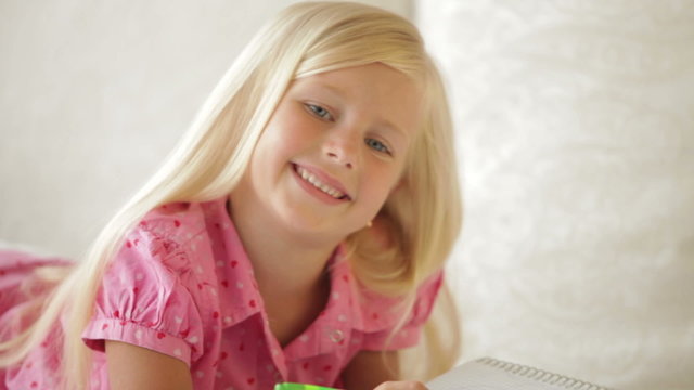 Happy little girl lying on couch writing in notebook and smiling