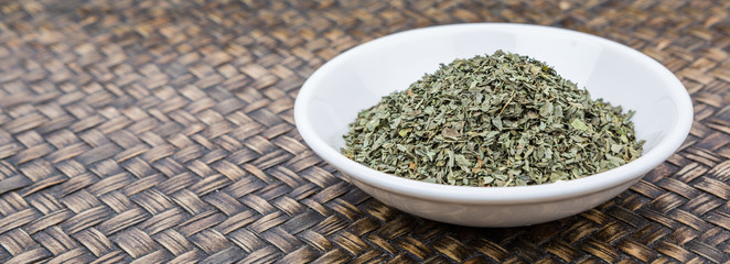 Dried basil leaves herbs over in white bowl over wooden background