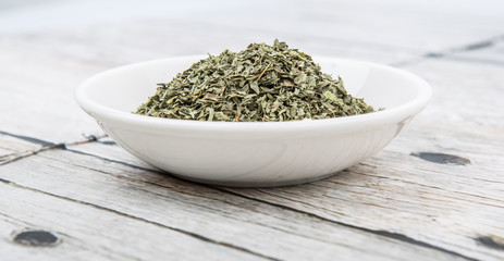 Dried basil leaves herbs over in white bowl over wooden background