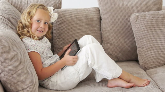 Little girl lying on couch and playing on tablet pc