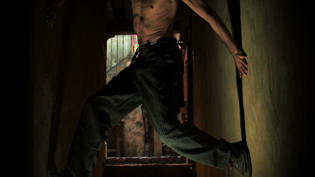 Strange orange glow of a shirtless stoned skinny man climbing up a narrow stone alley way.