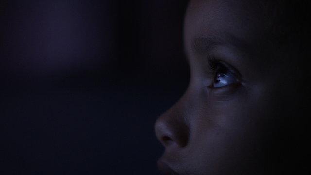 4K Close up of child's eyes watching a colourful screen in the dark