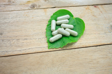 herbal medicine capsules with green herb leaf on wood table