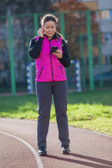 Woman listen the music with mobile phone while standing at the running track of the stadium