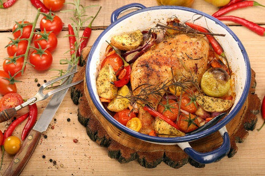 Roasted chicken legs with vegetables and herbs on wooden backgro