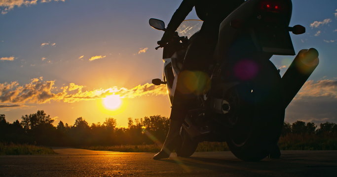 Businesswoman starting up her motorcycle and riding away towards sunset