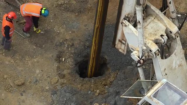Unrecognizable workers with hydraulic hammer drilling machine at construction site