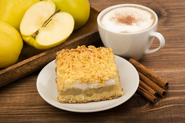 A piece of apple pie with cup of coffee and cinnamon sticks on the wooden background.