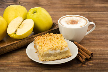 A piece of apple pie with cup of coffee and cinnamon sticks on the wooden background.