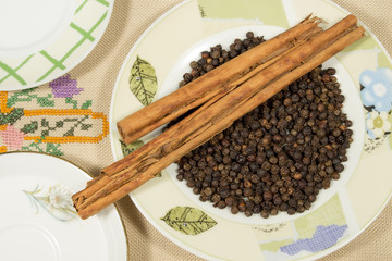 Several dishes on an embroidered cloth, one of them with black pepper grains and several cinnamon sticks