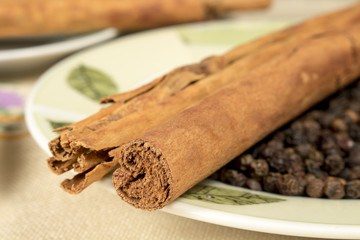 Close-up of cinnamon sticks and black pepper grains on decorated dish