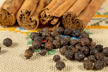 Grains of black pepper and several cinnamon sticks over a embroidered cloth