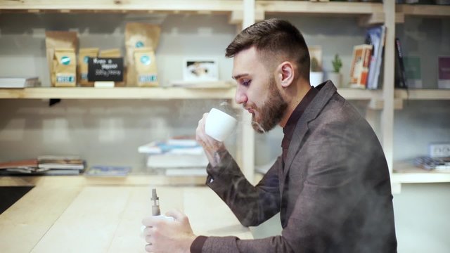 Bearded man in suit is smoking e-cigarette vape, chatting phone and drink coffee