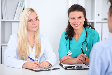 Two confident friendly female doctors sitting at the table and listen to the patient's history . Medical and health care concept