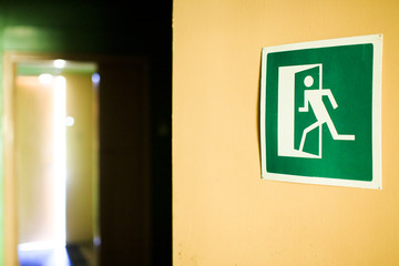 green emergency exit sign showing the open door in the distance. emergency exit sign indicating the way to the evacuation of the building. in the distance the light from the open door