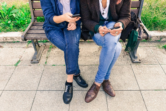 Couple of hipsters holding mobile phone - Two  trendy guys wifi connected sharing web content - Cropped human legs and hands with smartphone outdoors - Concept of modern business people taking a break