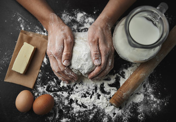 Woman hands kneading dough on the black board with eggs, milk, butter and flour. Healthy breakfast preparation concept.  - obrazy, fototapety, plakaty