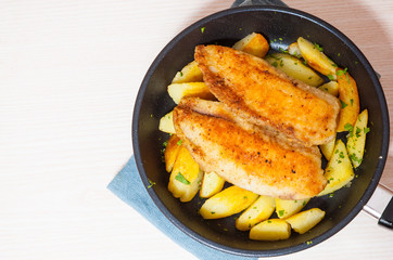 Fried fish fillet and potatoes in a frying pan