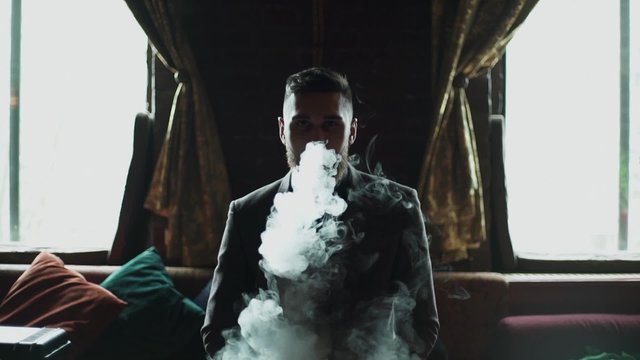 close-up of a bearded man in suit smoking electronic cigarette