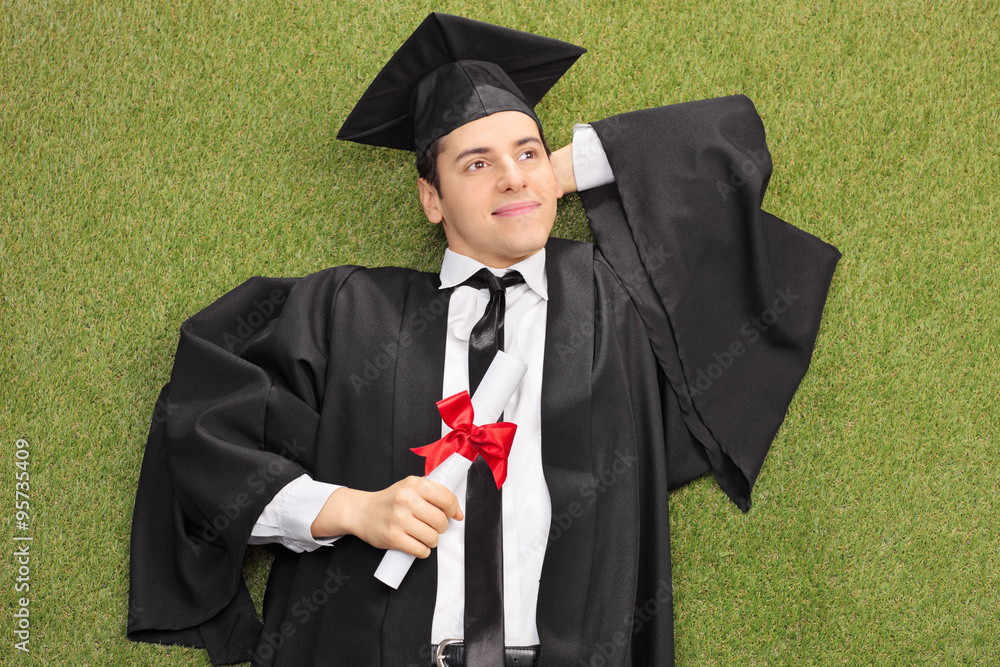 Wall mural Graduate lying on grass and daydreaming