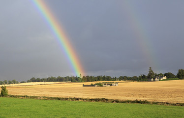 Beautiful rainbow in dark sky over field the harvest of wheat.