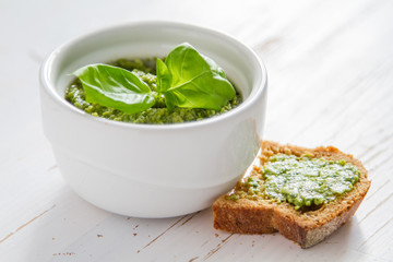 Pesto sauce in bowl, white wood background