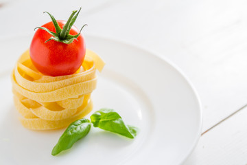 Dry pasta and cherry tomatoes, white wood background