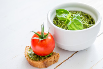 Pesto sauce in bowl, white wood background