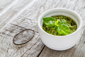Pesto sauce in bowl, rustic wood background