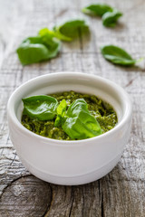 Pesto sauce in bowl, rustic wood background