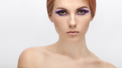 Closeup beauty portrait of a young beautiful redhead model with violet eyes makeup and naked shoulders
