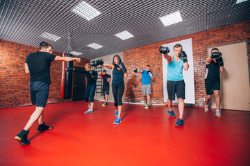 Boxing aerobox group with personal trainer man at fitness gym, gloves, punching bag