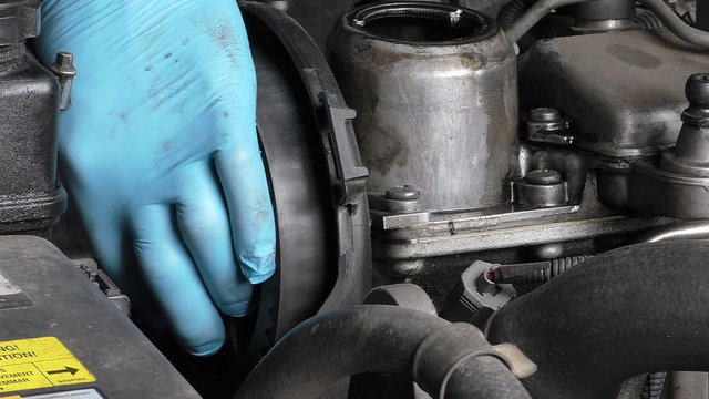 Car mechanic in gloves disassembling engine, unscrewing the last bolt and removing camshaft pulley
