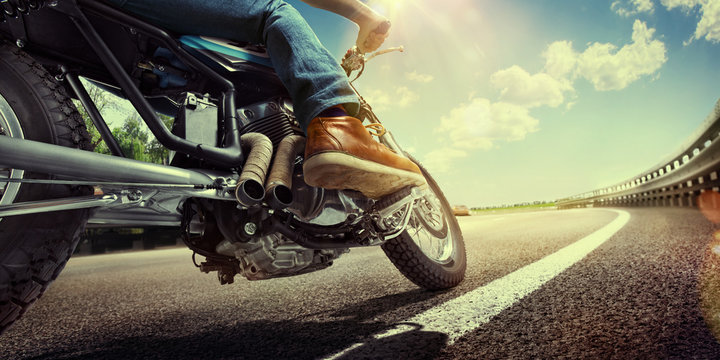 Fototapeta Biker riding motorcycle on an empty road at sunset